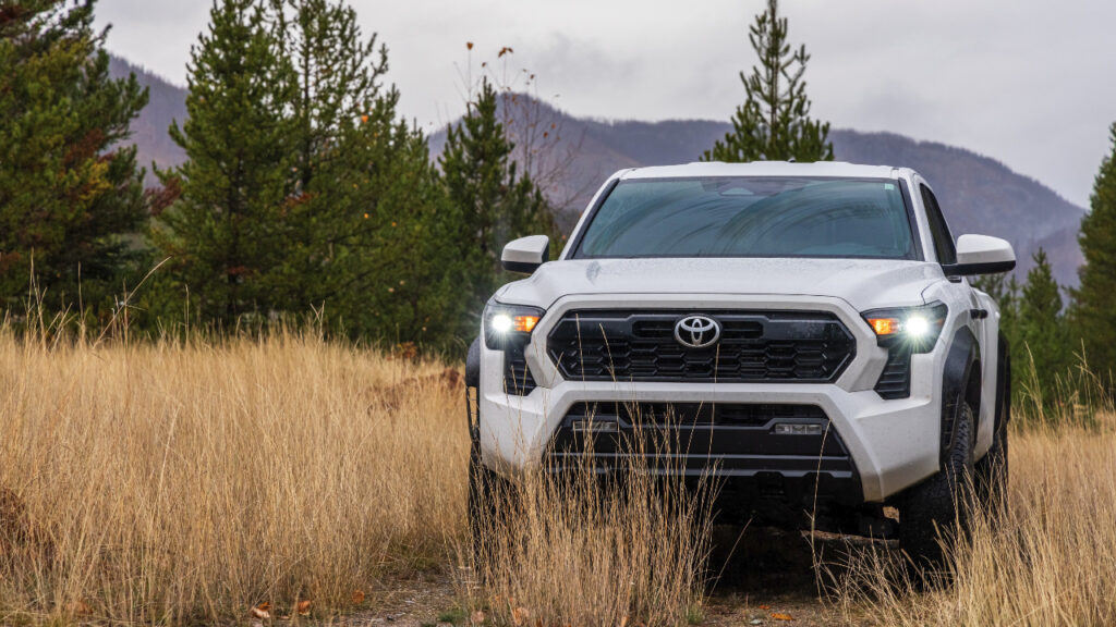 A white 2024 Toyota Tacoma TRD Off-Road parked amidst wet grass in a scenic, rainy forest setting.