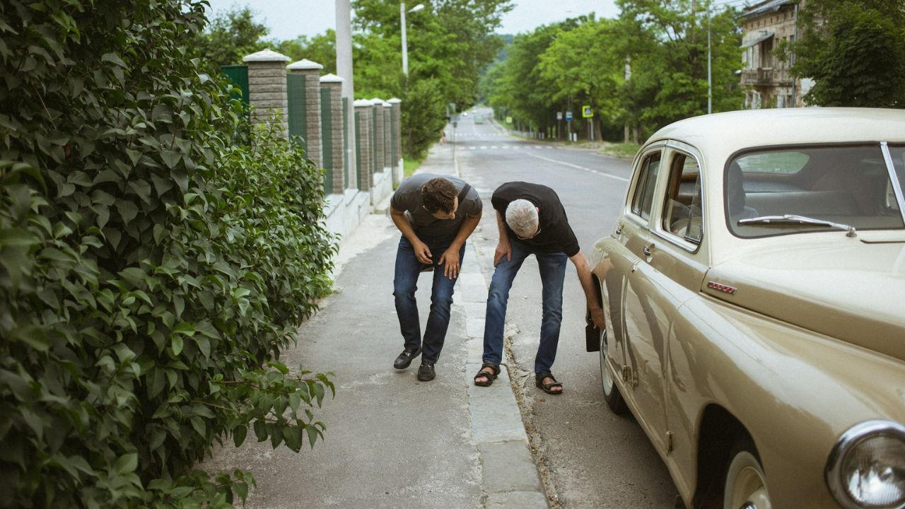 Two men checking tires of a car