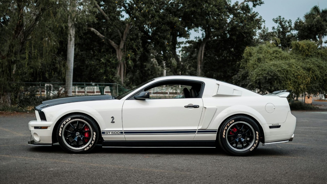 Side view of a classic white Ford Mustang GT500 parked in a serene outdoor setting.