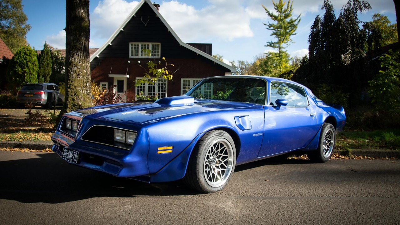 A striking blue vintage car parked in a suburban neighborhood on a sunny day.
