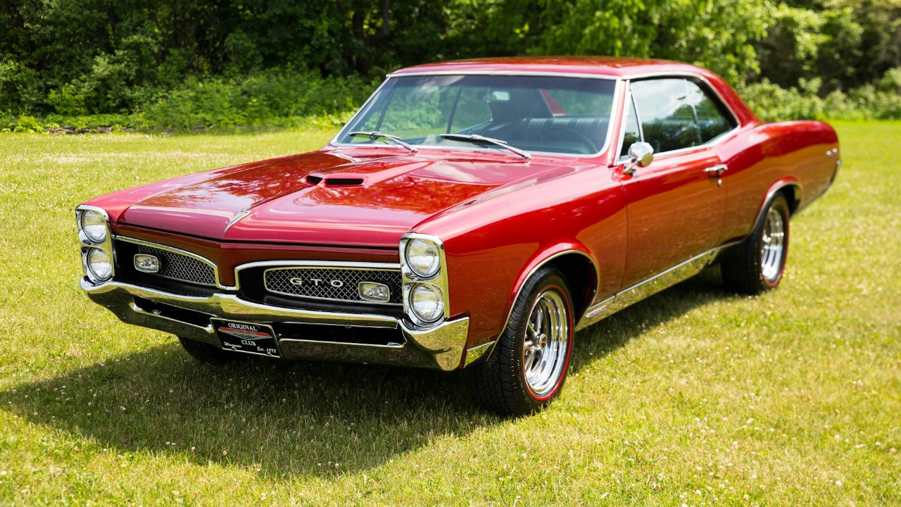 Vintage red Pontiac GTO car parked outdoors in a sunny Rockton field.