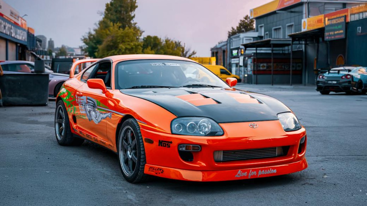A vivid orange Toyota Supra parked in an open area of Ankara, Türkiye, during a calm day.
