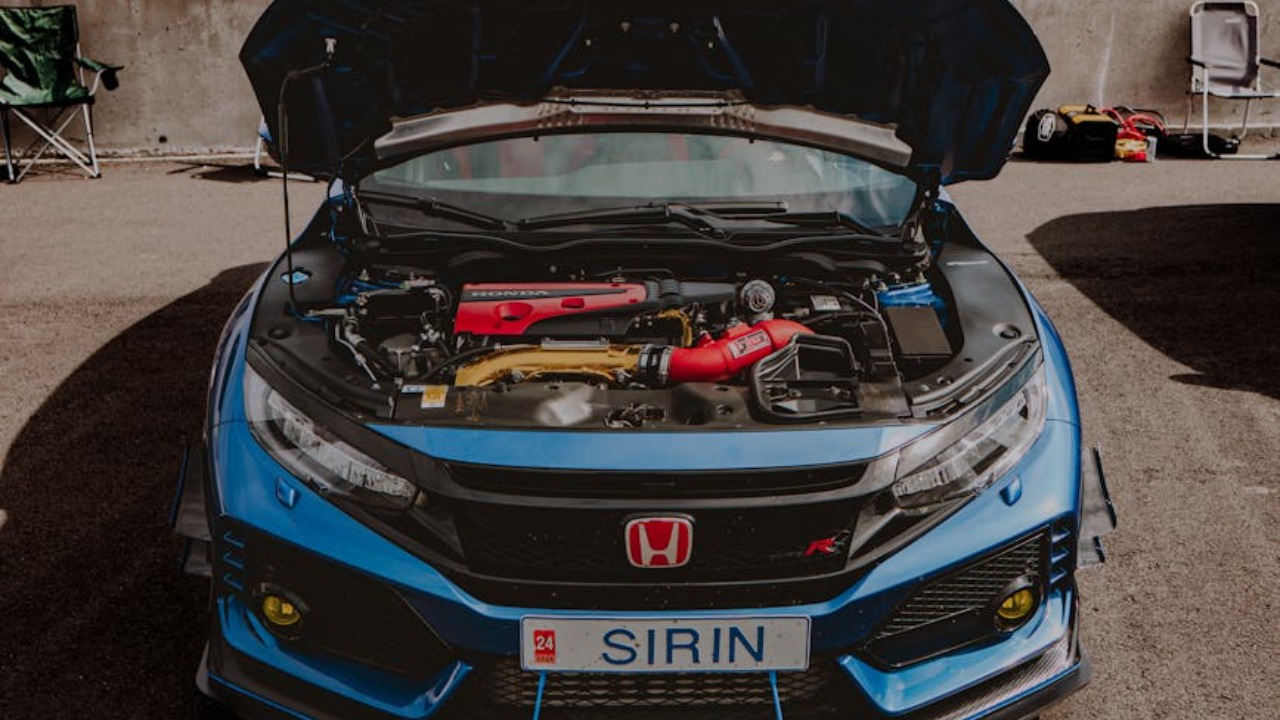 Blue Honda Civic Type R with open hood, displaying engine at a racetrack.