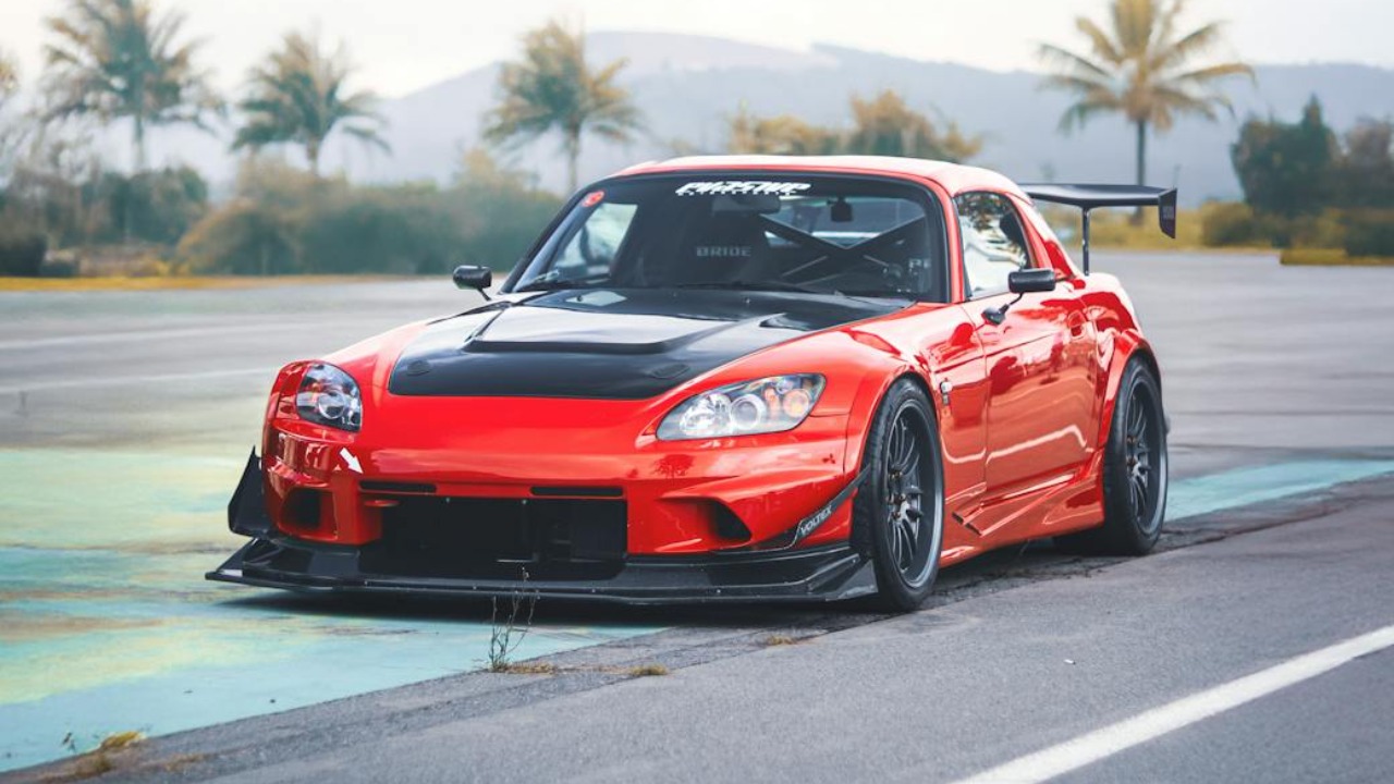 A sleek red Honda car with a black hood, parked outdoors with palm trees, showcasing modern automotive design.