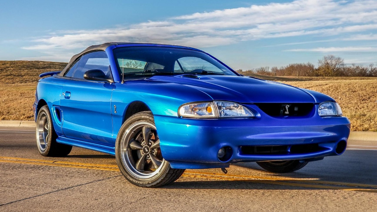 Classic 1998 blue Ford Mustang convertible captured on a sunny Texas road.