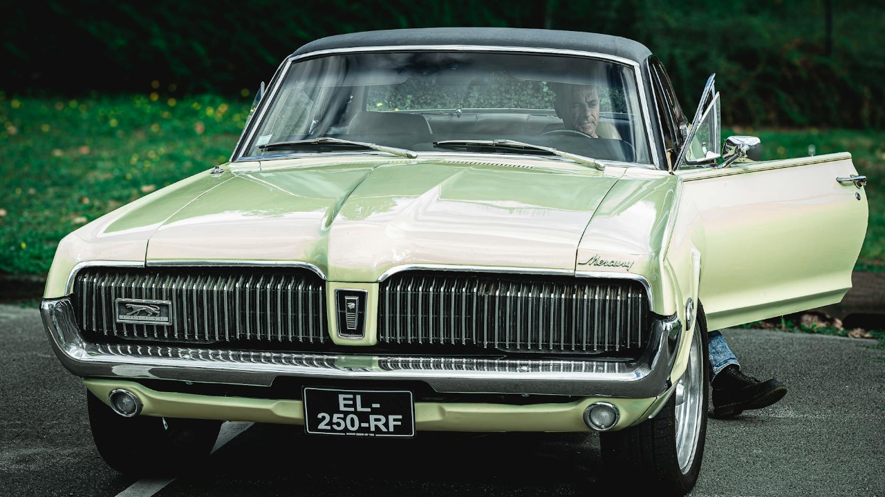 Classic Mercury Cougar with open door and driver outdoors.