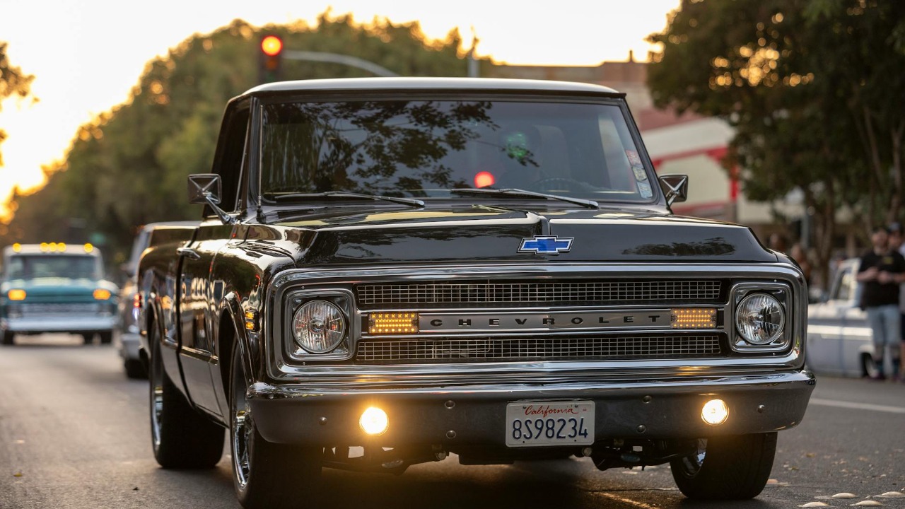 Vintage Chevrolet C/K pickup truck driving on a city street at sunset with California plates.