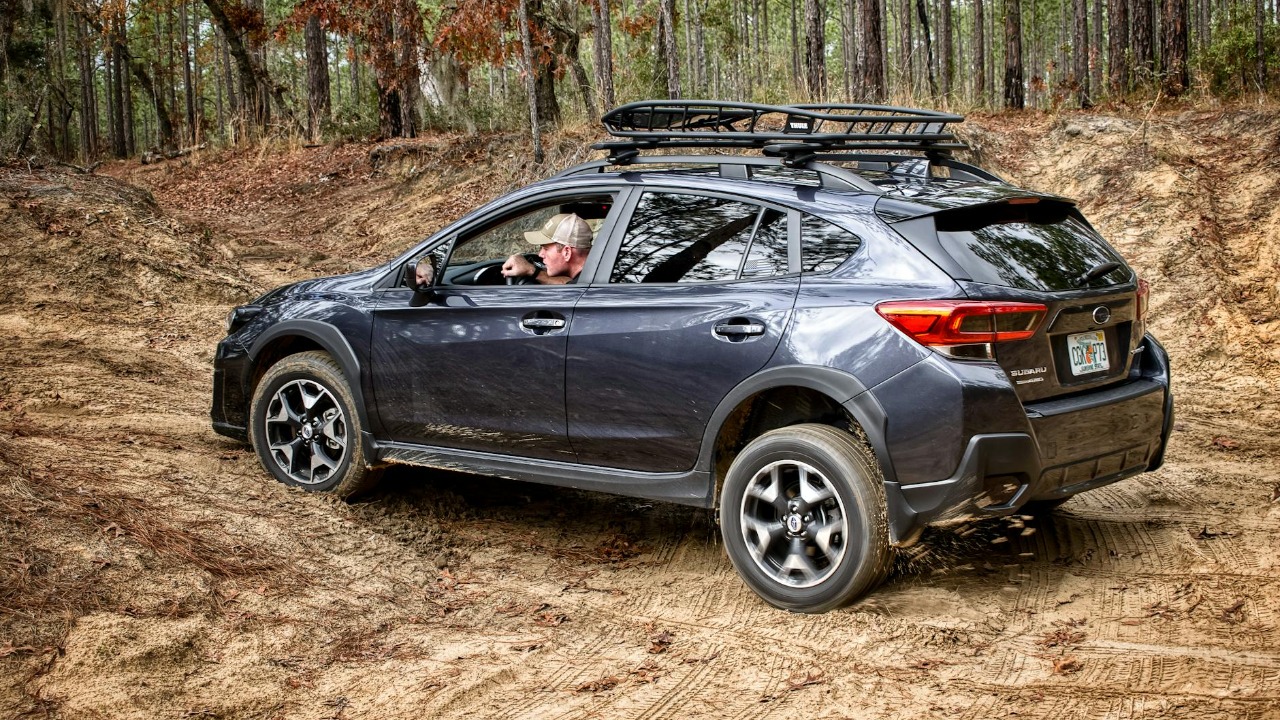 A man driving a Subaru on a rugged dirt road through a forest, showcasing off-road capabilities.