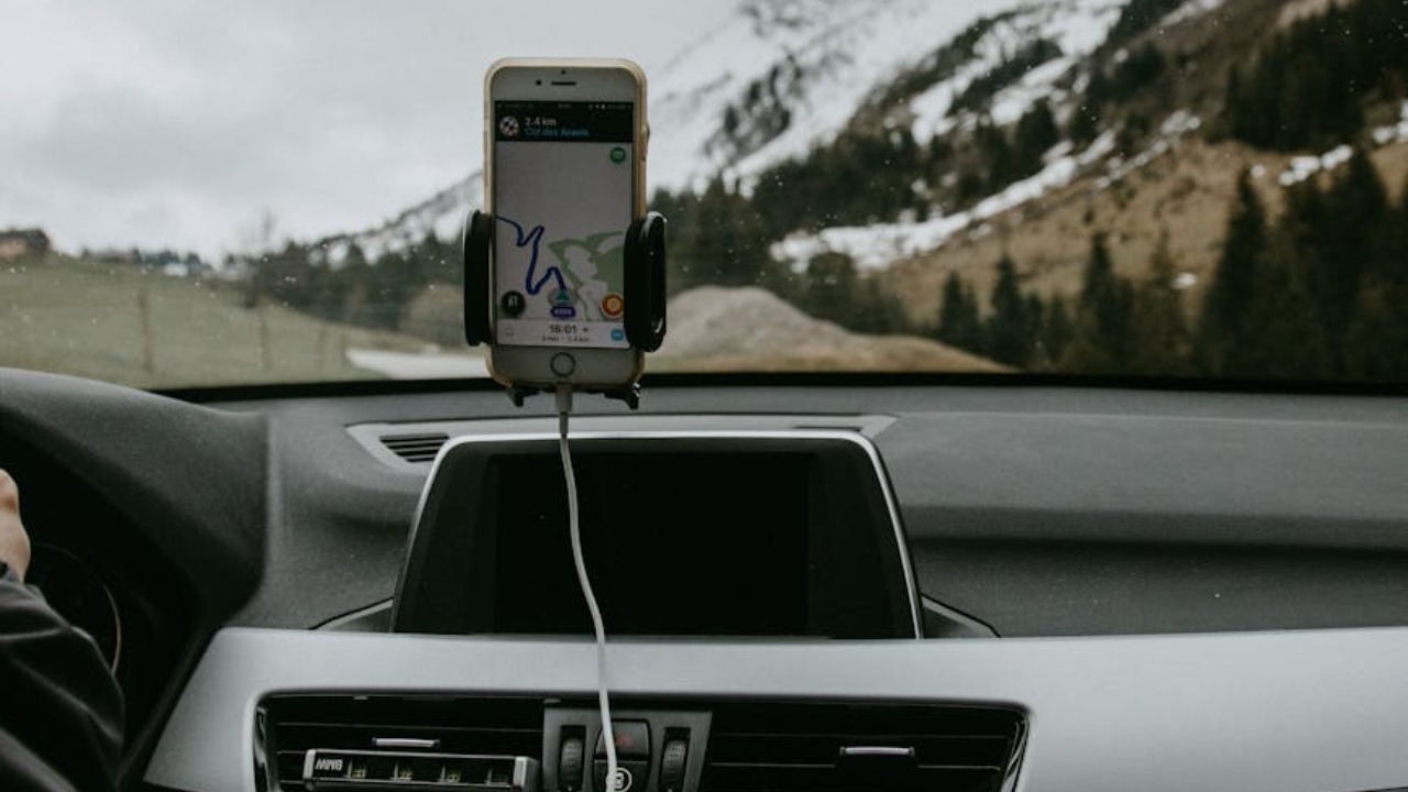 Driver in car with smartphone showing route due to GPS against snowy hill slope with coniferous trees and road