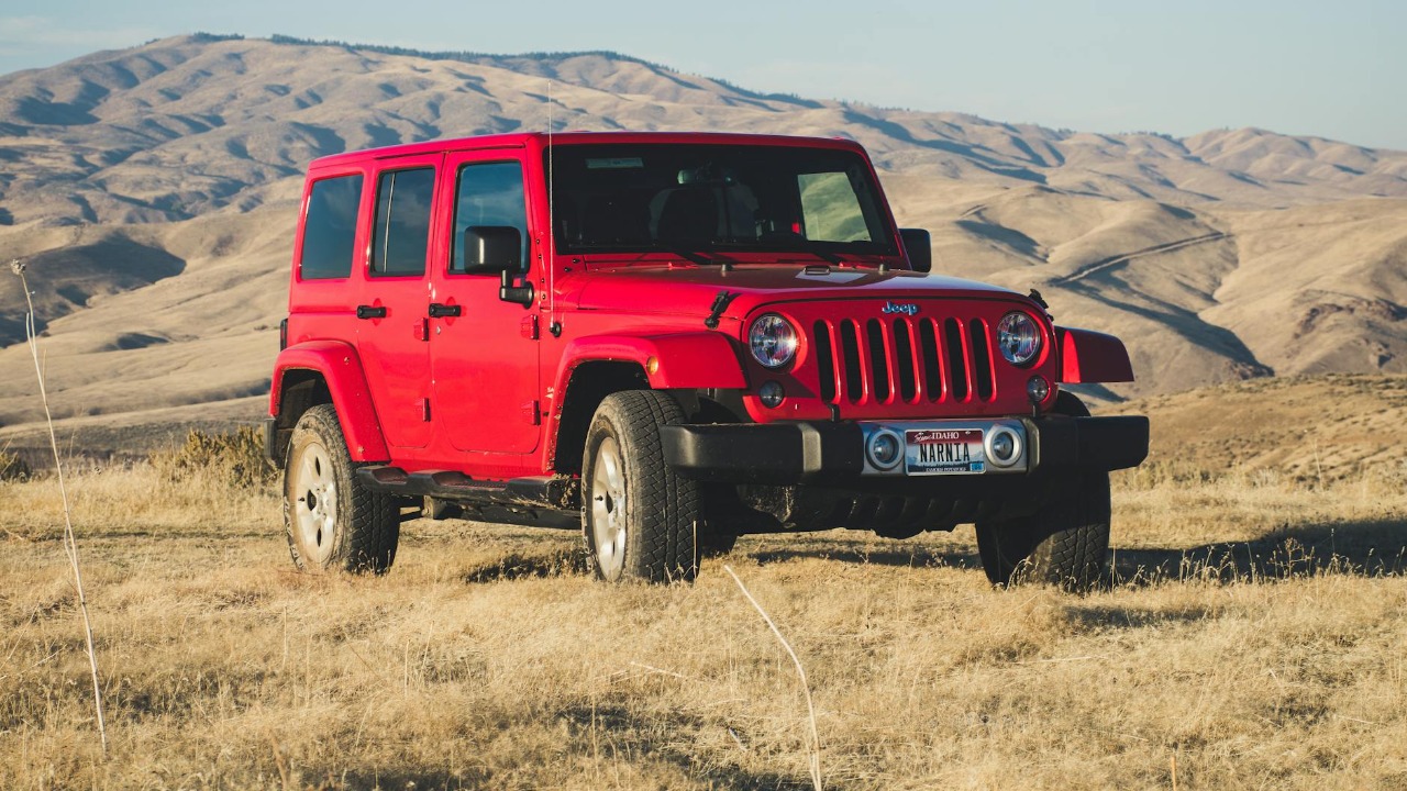A striking red Jeep Wrangler parked in a vast, desert-like landscape under a clear sky.