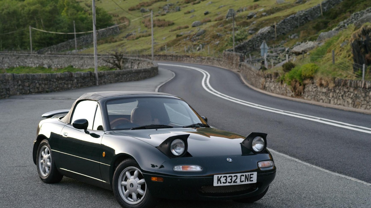 A sleek black sports car parked on a scenic winding mountain road with lush greenery.