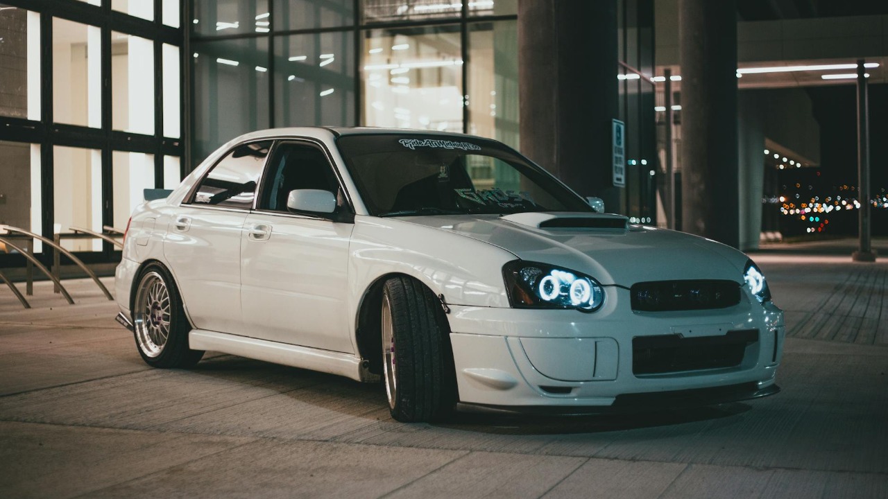 A sleek modified white Subaru Impreza WRX STI parked in an urban setting at night.