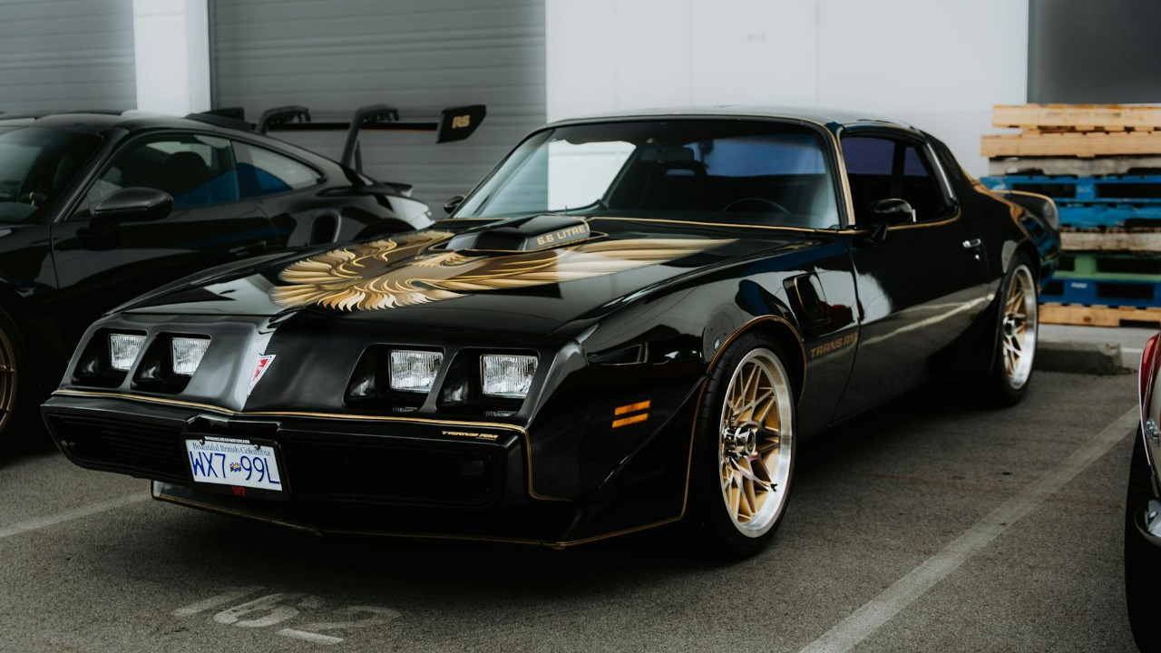 A vintage black Pontiac Firebird with golden decals parked in an indoor lot, showcasing its iconic style.