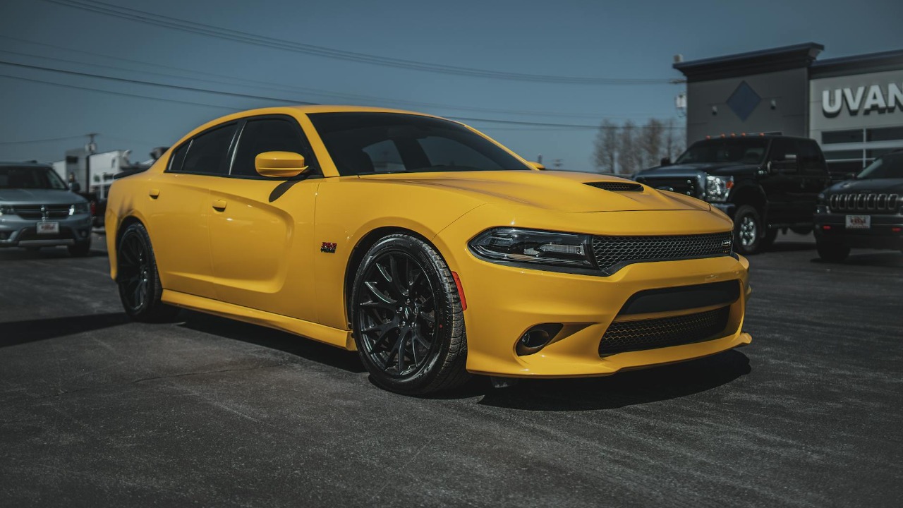 A vibrant yellow Dodge Charger parked outdoors at a car dealership on a sunny day.