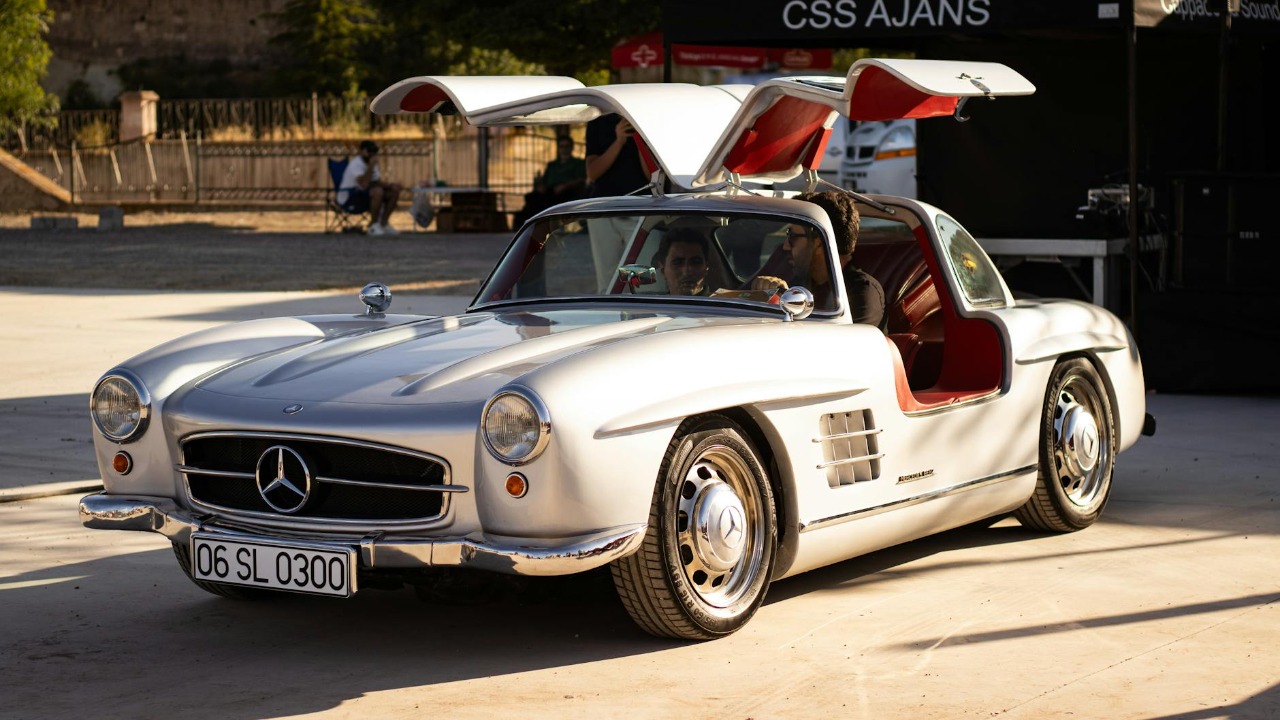 Silver Mercedes-Benz 300SL with iconic gullwing doors under sunlight at outdoor event.