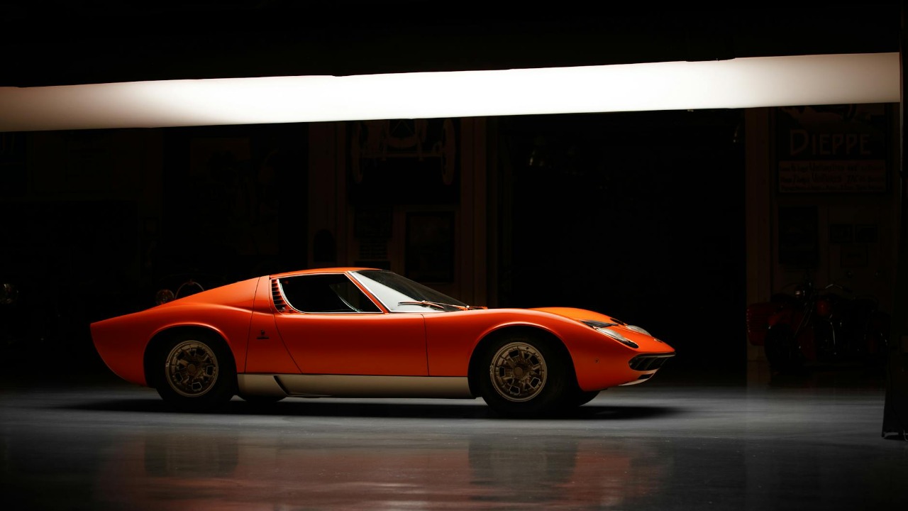 Side profile of a vintage Lamborghini Miura under studio lights, showcasing its retro design.