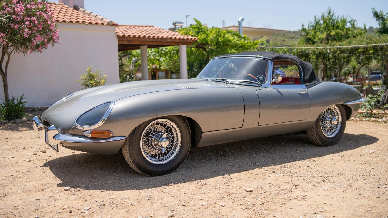 Vintage Jaguar E-Type convertible parked in a sunny yard, showcasing luxury and nostalgia.