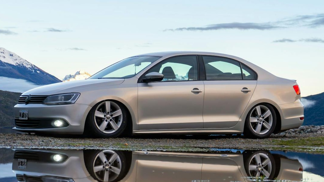 A Volkswagen Jetta parked near Lago Puelo, Chubut, Argentina, reflecting in a puddle with mountain views.