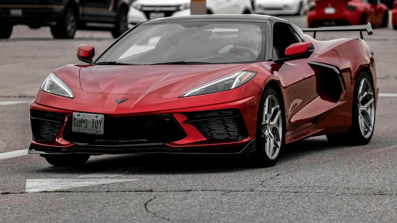 Dynamic shot of a red Chevrolet Corvette C8 in a busy urban parking lot during the day.