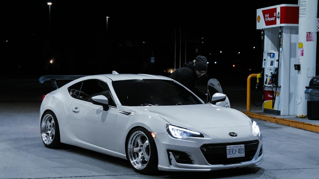 A sleek white Subaru BRZ parked at a brightly lit gas station during the night.