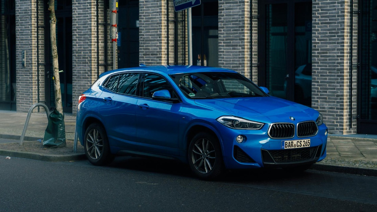 A vibrant blue SUV is parked against an urban brick wall, showcasing a sleek and modern design.