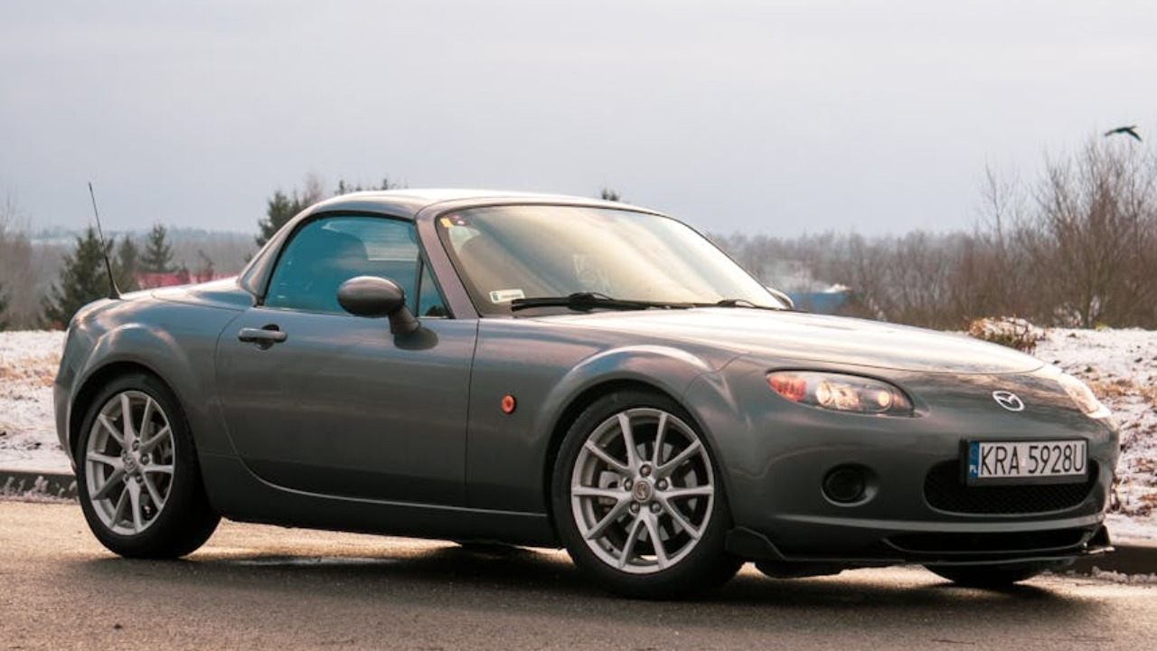 Silver Mazda Miata MX-5 parked on a snowy road in Kraków during the day.
