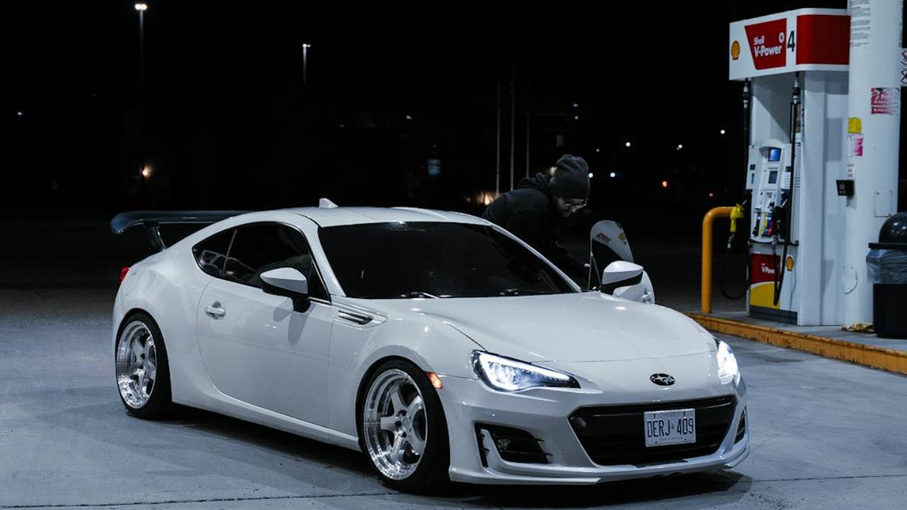 A sleek white Subaru BRZ parked at a brightly lit gas station during the night.