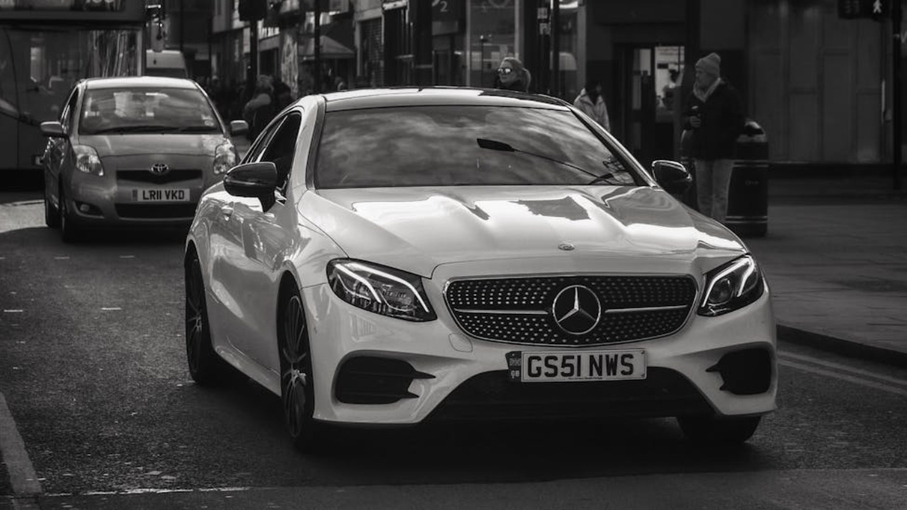 Monochrome image of a Mercedes-Benz driving on an urban street, capturing the elegance of the car in motion.