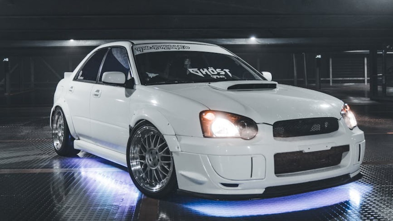A white Subaru WRX with neon lights showcased in a dimly lit parking garage.