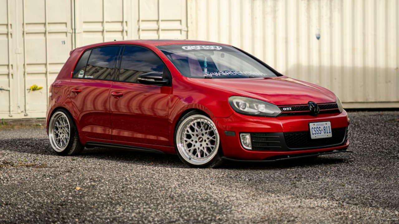 A striking red Volkswagen Golf GTI parked near industrial shipping containers in London, Canada.