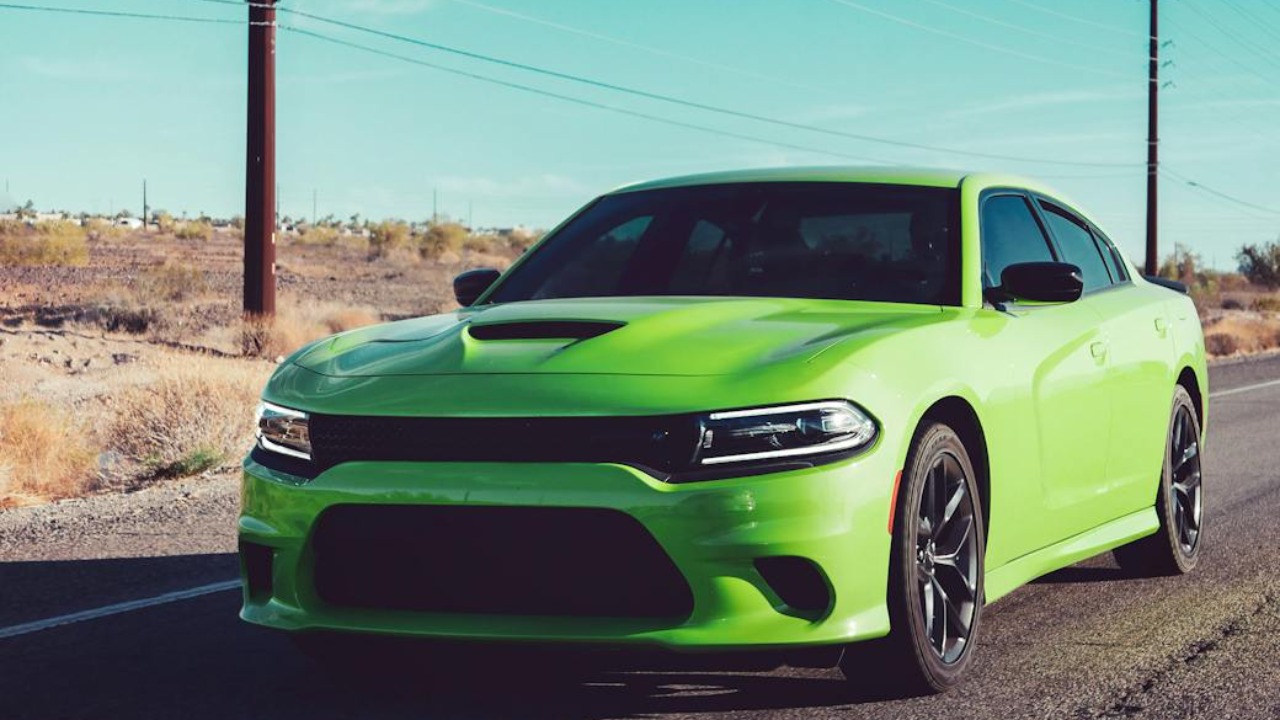 A bright green sports car speeding on a sunny rural road under clear skies.