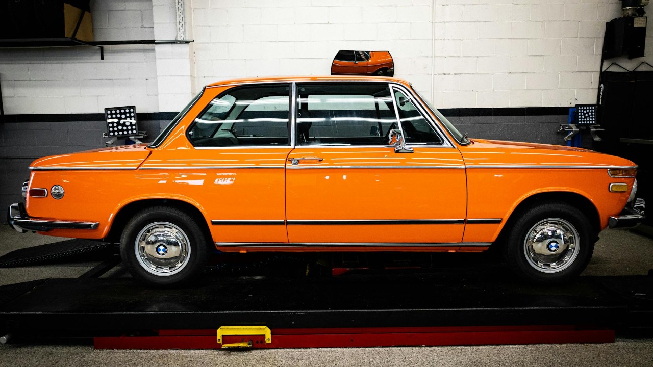 Bright orange vintage BMW 2002 parked indoors showcasing classic automotive design.