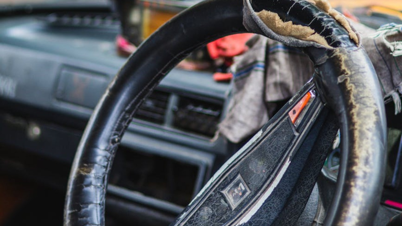 Detailed view of a vintage car's worn interior showcasing a frayed steering wheel and retro decor.