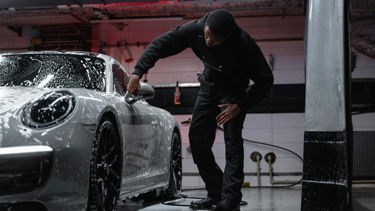 Man washing a luxury car in an indoor garage, emphasizing automotive care.