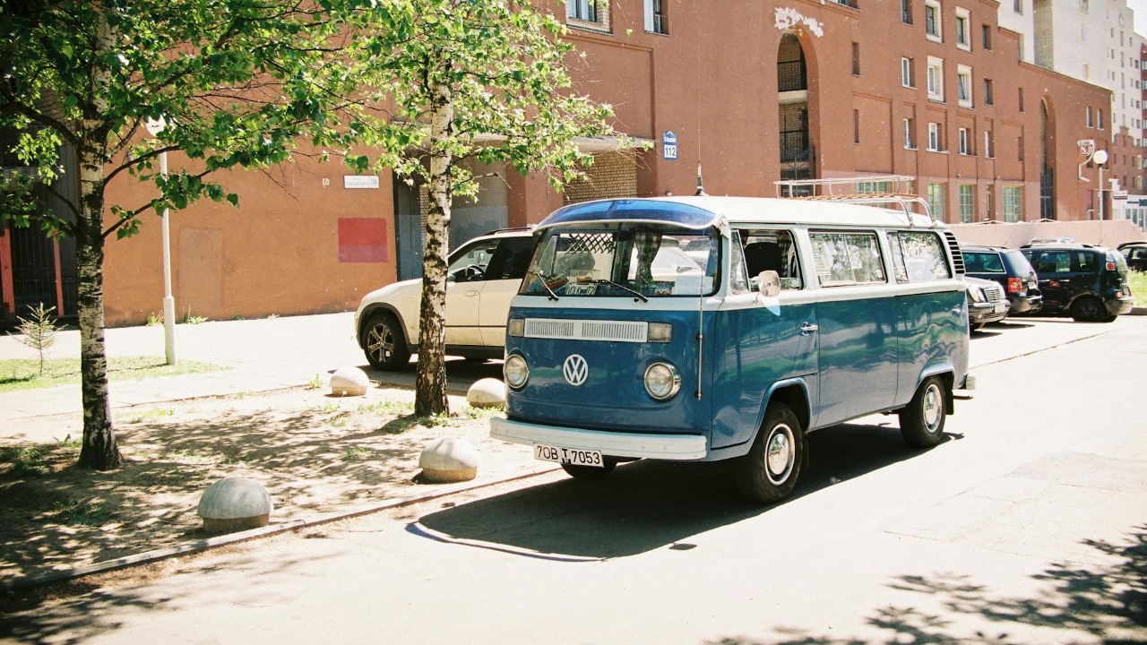 A classic blue Volkswagen van parked on a sunny street in an urban setting.