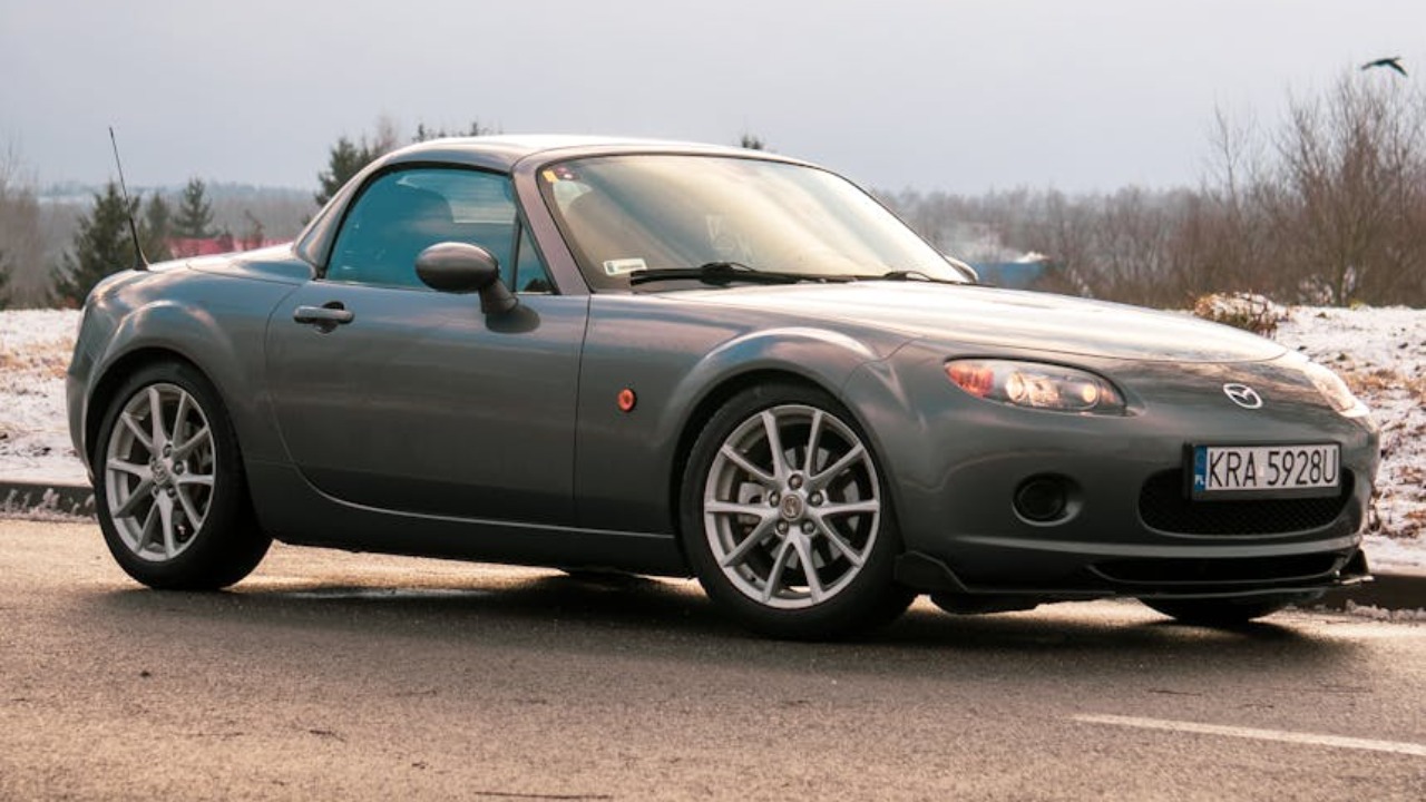 Silver Mazda Miata MX-5 parked on a snowy road in Kraków during the day.