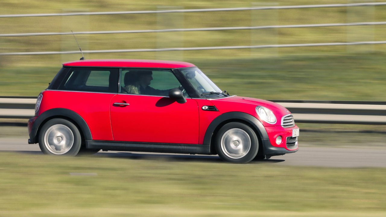 A red Mini Cooper car in motion captured on a road in Jönköping, Sweden.