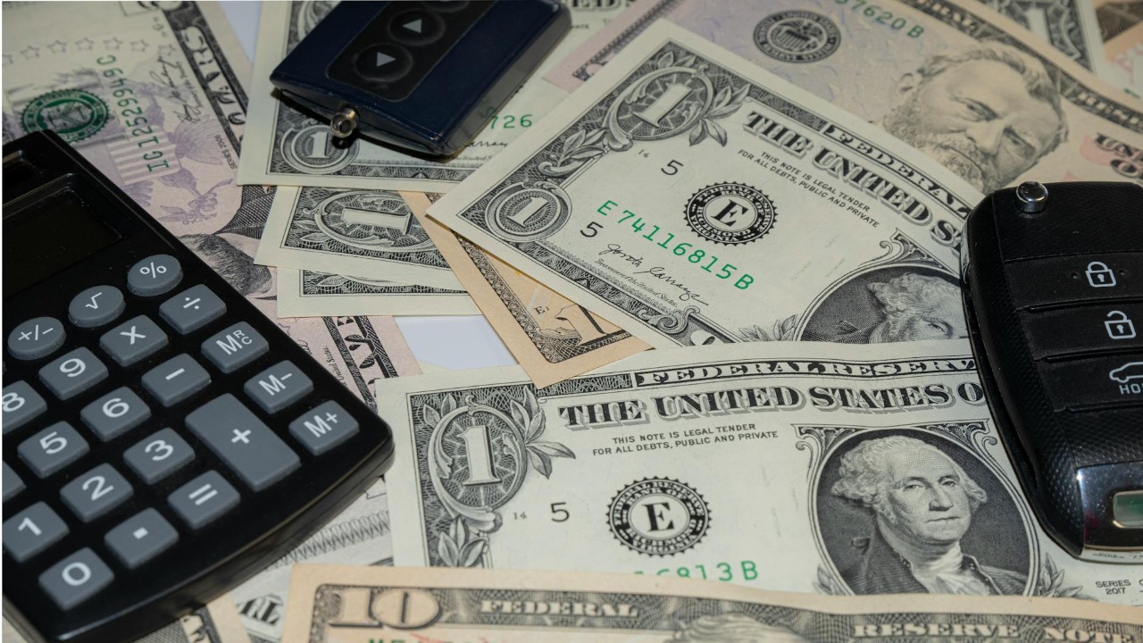 Close-up of various US banknotes, calculator, and car key illustrating finance concept.