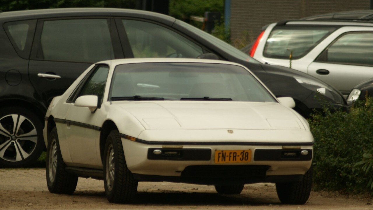 A white 1984 Pontiac Fiero, whose plastic panels hang on the Fiero space frame